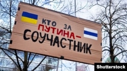 Плакат російською мовою «Хто за Путіна – той співучасник» на демонстрації проти війни Росії в Україні, Ганновер, Німеччина, 9 квітня 2022 року