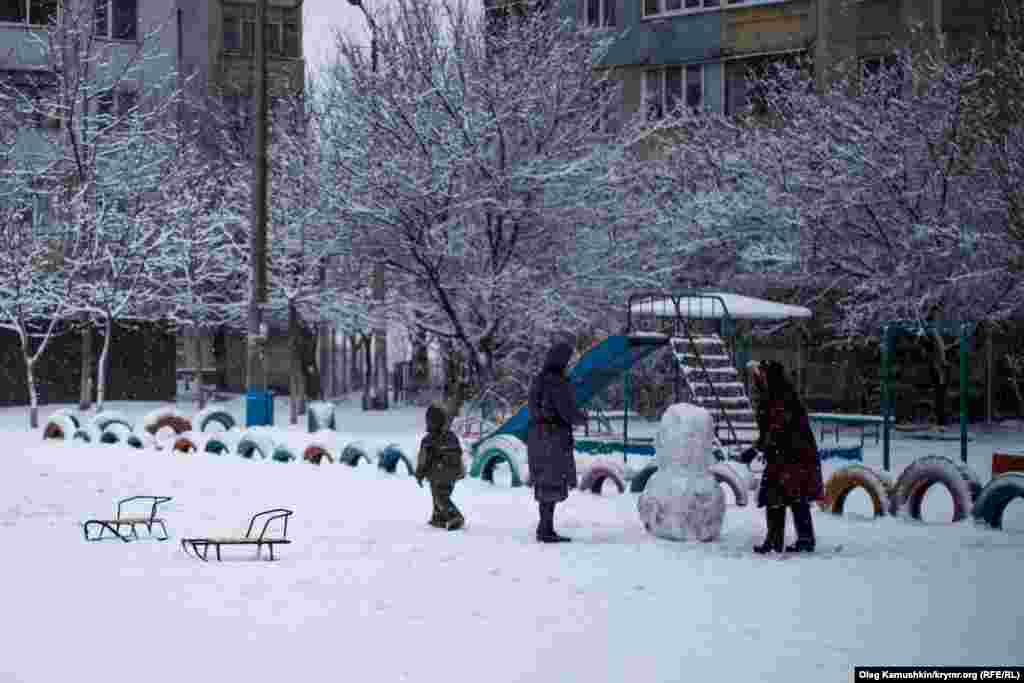 Поки діти грають, дорослі ліплять сніговика.